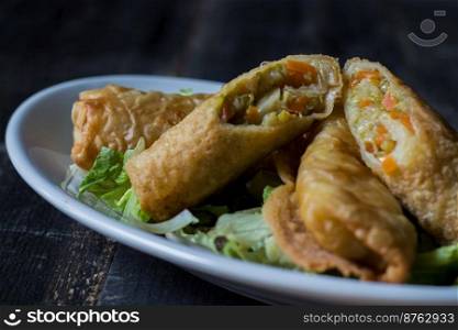 Homemade spring rolls on a bed of lettuce. In a white plate on a wooden background
