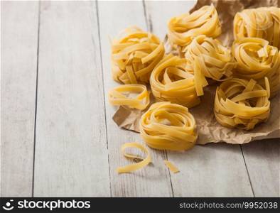 Homemade tagliatelle pasta in brown paper on white wooden background. 
