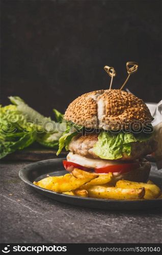 Homemade tasty burger with chicken, lettuce, mozzarella and tomatoes on rustic kitchen table background, front view