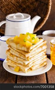 Homemade thin crepes with orange jam, stack of pancakes on wooden rustic background