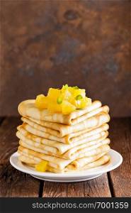 Homemade thin crepes with orange jam, stack of pancakes on wooden rustic background