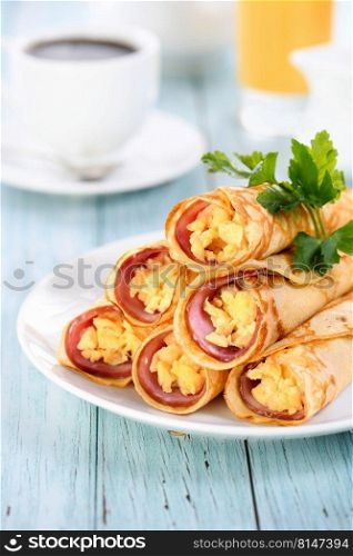 Homemade thin pancakes with a slice of ham and scrambled eggs, stacked in a stack, on the table. Great breakfast idea.