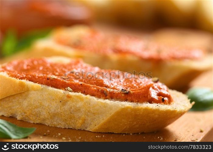 Homemade tomato-butter spread on baguette slices with fresh ground pepper on wooden board (Selective Focus, Focus on the front of the spread)