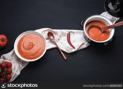 Homemade tomato cream soup and hot peppers on a kitchen towel and black table. Above view of red vegetable soup. Vegetarian meal. Healthy eating.