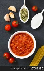 Homemade traditional Italian marinara or pomodoro tomato sauce made of fresh tomato, garlic, dried oregano and salt, served in bowl with ingredients on the side, photographed overhead on slate with natural light (Selective Focus, Focus on the top of the sauce)