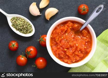 Homemade traditional Italian marinara or pomodoro tomato sauce made of fresh tomato, garlic, dried oregano and salt, served in bowl with ingredients on the side, photographed overhead on slate with natural light (Selective Focus, Focus on the top of the sauce)