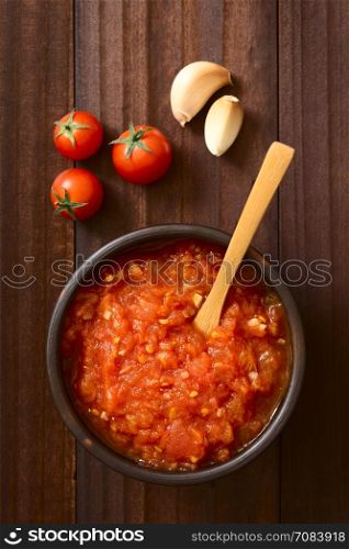 Homemade traditional Italian marinara or pomodoro tomato sauce made of fresh tomato, garlic, dried oregano and salt, served in rustic bowl with ingredients on the side, photographed overhead on dark wood with natural light (Selective Focus, Focus on the top of the sauce)