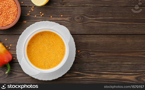 Homemade Turkish lentil soup (Merdzimek Chorbasy). Red lentil soup on a dark wooden table, ingredients for the soup next to a plate. Healthy and wholesome food. Top view, copy space