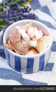 Homemade vanilla and chocolate ice cream with marshmallow, served in ceramic bowl on white wooden background.