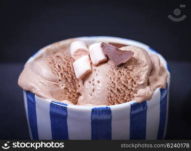 Homemade vanilla and chocolate ice cream with marshmallow, served in ceramic bowl on dark background.