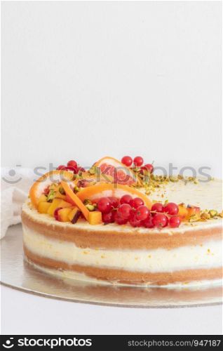 Homemade vanilla birthday cake decorated with orange, peach and gooseberries isolated on table tob. Celebration, party cake.