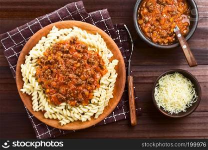 Homemade vegan bolognese sauce made with soy meat, fresh tomatoes, onion and garlic served on fusilli pasta on wooden plate, sauce and grated cheese on the side, photographed overhead. Vegan Soy Meat Bolognese Sauce on Pasta