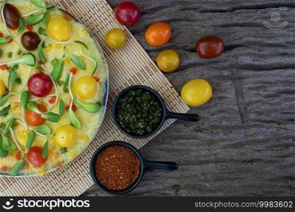 Homemade vegetable pizza with cherry tomatoes and other ingredients on a wooden background