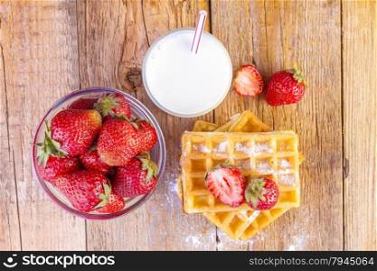 homemade waffles with strawberries and glass with milk on wooden background