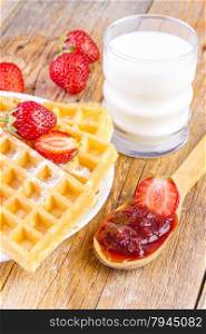 homemade waffles with strawberries maple syrup and glass with milk on wooden background
