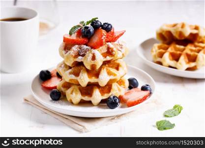 homemade waffles with syrup and fresh berries on white wooden table