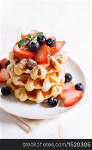 homemade waffles with syrup and fresh berries on white wooden table