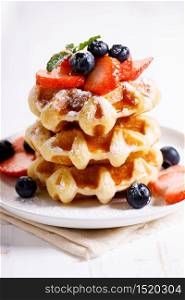 homemade waffles with syrup and fresh berries on white wooden table, closeup