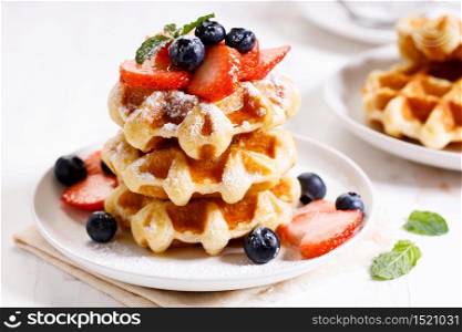 homemade waffles with syrup and fresh berries on white wooden table, closeup
