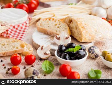 Homemade wheat bread with quail eggs and raw wheat and fresh tomatoes on wood background. Classic italian village food. Garlic, black and green olives. Wooden spatula
