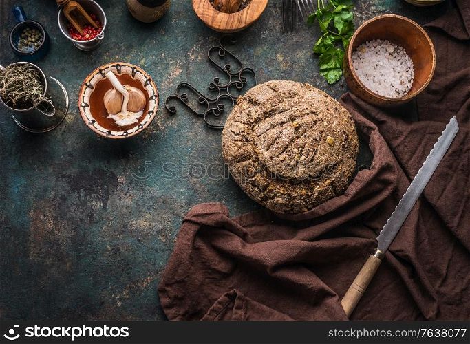 Homemade whole grain bread on dark kitchen table background with knife and cooking tools and ingredients. Top view. Place for text