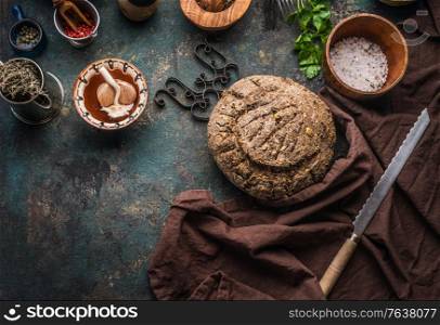 Homemade whole grain bread on dark kitchen table background with knife and cooking tools and ingredients. Top view. Place for text