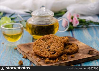 Homemade wholegrain cookies with raisin on wooden cutting board with tea and teapot on blue wooden table