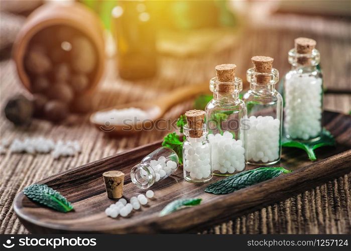 Homeopathic globules in small bottles with mint leaves and wooden spoon in background