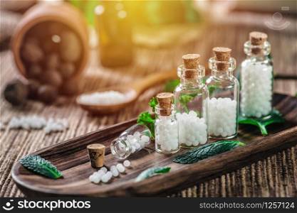 Homeopathic globules in small bottles with mint leaves and wooden spoon in background