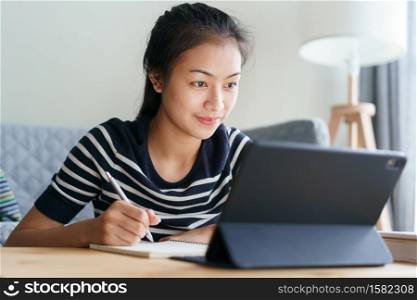 Homework. student Asian woman using tablet while sitting in the living room at home, Concept of online learning at home