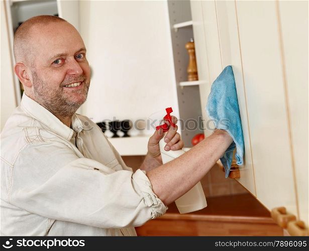 Homeworks, smiling man used a cleaning cloth and a detergent spray, he cleaning the kitchen cupboard door