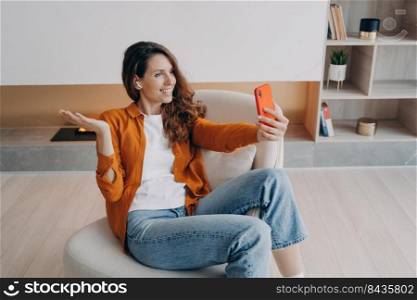 Homey caucasian girl has video phone call. Relaxed young woman is using airpods and cellphone at home. Wireless earphones using at online meeting. Technology using, leisure and communication concept.. Homey caucasian girl has video phone call. Relaxed young woman is using airpods and cellphone.