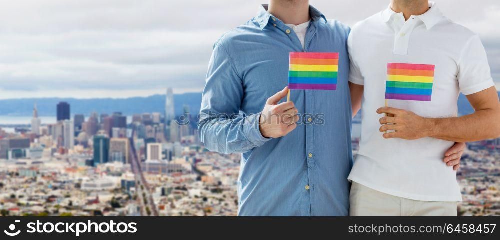 homosexual and gay pride concept - close up of happy male couple with rainbow flags hugging over san francisco city view background. male couple with gay pride flags at san francisco