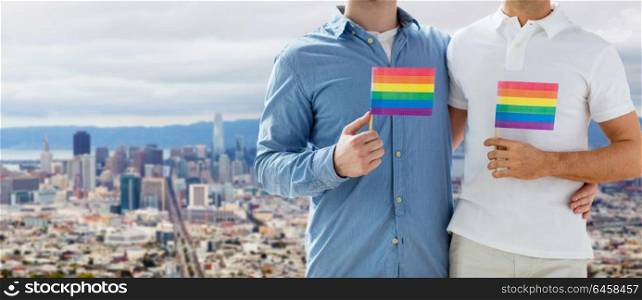 homosexual and gay pride concept - close up of happy male couple with rainbow flags hugging over san francisco city view background. male couple with gay pride flags at san francisco