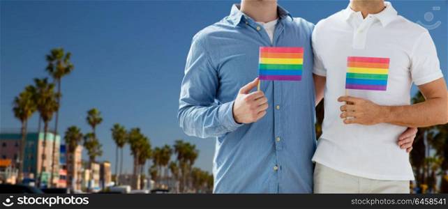 homosexual and gay pride concept - close up of happy male couple with rainbow flags hugging over venice beach in los angeles background. male couple with gay pride flags in los angeles