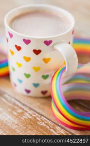 homosexual and lgbt concept - close up of cup with rainbow colored heart pattern and gay pride awareness ribbon on wooden table. cup with heart pattern and gay awareness ribbon. cup with heart pattern and gay awareness ribbon