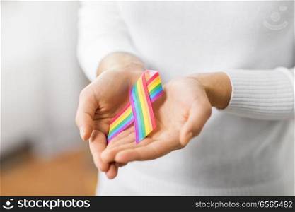 homosexual and lgbt concept - close up of female hands holding gay pride awareness ribbon. female hands holding gay pride awareness ribbon