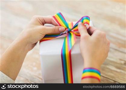 homosexual and lgbt concept - close up of female hands packing gift box and tying bow of gay pride awareness ribbon. female hands and present with gay awareness ribbon. female hands and present with gay awareness ribbon