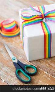 homosexual and lgbt concept - close up of gift box, gay pride awareness ribbon and scissors on wooden table. present, gay awareness ribbon and scissors. present, gay awareness ribbon and scissors