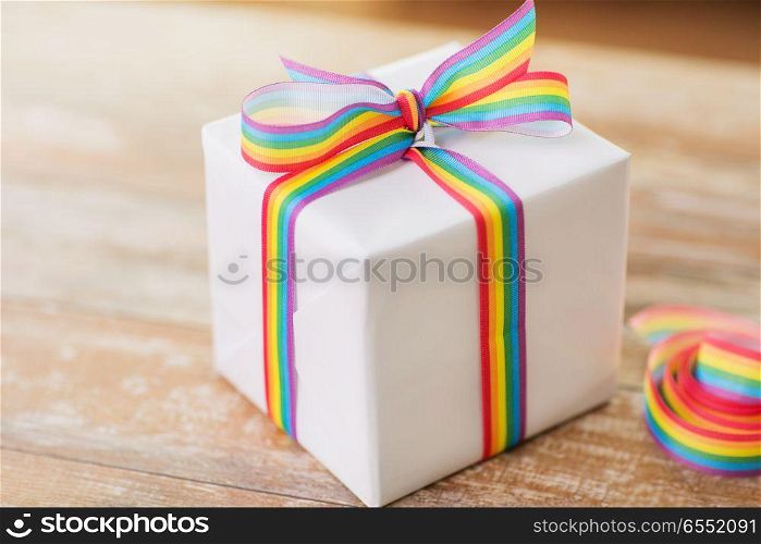 homosexual and lgbt concept - close up of gift box with gay pride awareness ribbon on wooden table at home. close up of gift box with gay awareness ribbon. close up of gift box with gay awareness ribbon