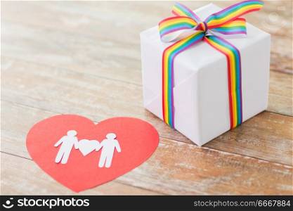 homosexual and lgbt concept - close up of gift box with gay pride awareness ribbon and male couple pictogram on red paper heart on wooden boards. gift with gay awareness ribbon and male pictogram. gift with gay awareness ribbon and male pictogram