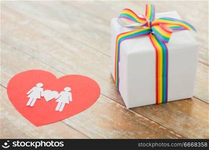 homosexual and lgbt concept - close up of gift box with gay pride awareness ribbon and female couple pictogram on red paper heart on wooden boards. gift with gay awareness ribbon and woman pictogram. gift with gay awareness ribbon and woman pictogram