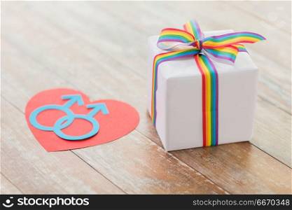 homosexual and lgbt concept - close up of gift box with gay pride awareness ribbon and male gender symbol on heart on wooden boards. gift with gay awareness ribbon and mars symbol. gift with gay awareness ribbon and mars symbol