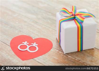 homosexual and lgbt concept - close up of gift box with gay pride awareness ribbon and female gender symbol on red heart on wooden boards. gift with gay awareness ribbon and venus symbol. gift with gay awareness ribbon and venus symbol