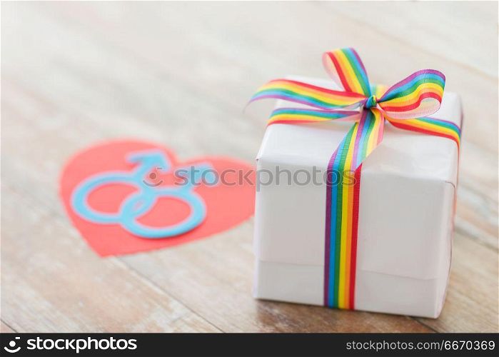 homosexual and lgbt concept - close up of gift box with gay pride awareness ribbon and male gender symbol on wooden boards. close up of gift box with gay awareness ribbon. close up of gift box with gay awareness ribbon