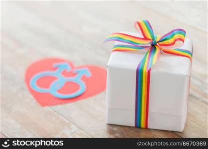 homosexual and lgbt concept - close up of gift box with gay pride awareness ribbon and male gender symbol on wooden boards. close up of gift box with gay awareness ribbon. close up of gift box with gay awareness ribbon