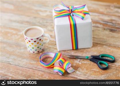 homosexual and lgbt concept - cup of coffee or cacao drink with gift box, gay pride awareness ribbon and scissors on wooden table. cacao, gift, gay awareness ribbon and scissors. cacao, gift, gay awareness ribbon and scissors
