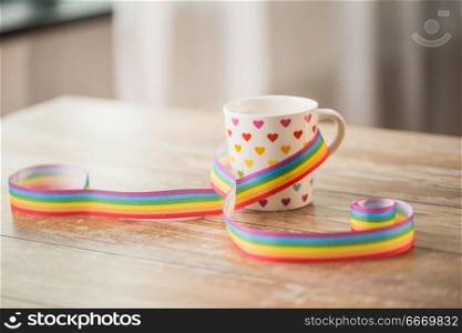 homosexual and lgbt concept - cup with rainbow colored heart pattern and gay pride awareness ribbon on wooden table. cup with heart pattern and gay awareness ribbon. cup with heart pattern and gay awareness ribbon
