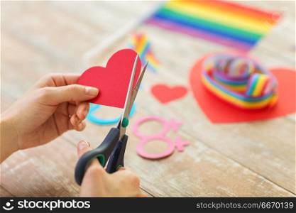 homosexual and lgbt concept - female hands with scissors cutting out red paper heart decoration for gay party. hands making heart decoration for gay party. hands making heart decoration for gay party
