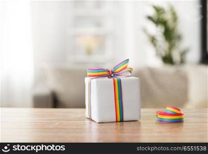 homosexual and lgbt concept - gift box with gay pride awareness ribbon on wooden table at home. present with gay awareness ribbon on table at home. present with gay awareness ribbon on table at home